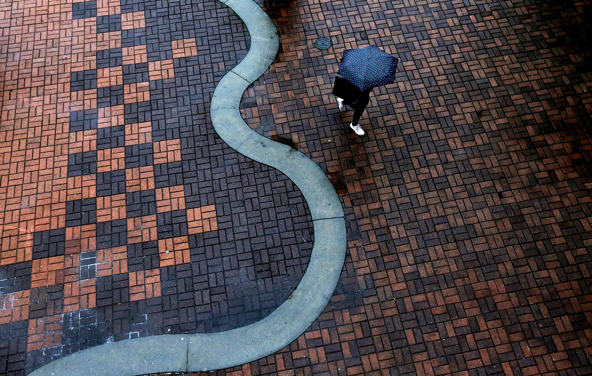 A pedestrian walks with an umbrella on a rainy day in Long Beach. 
