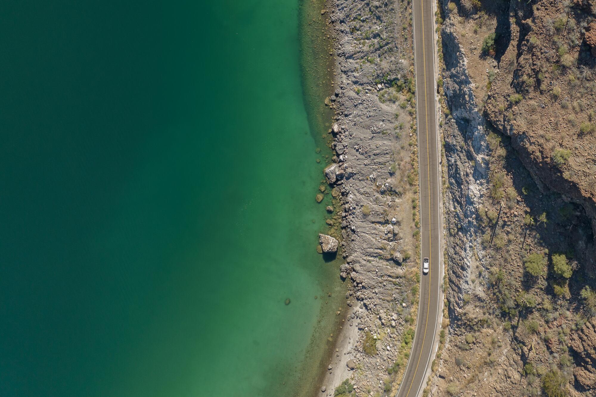 A drone photo of a car driving along a coastal highway.