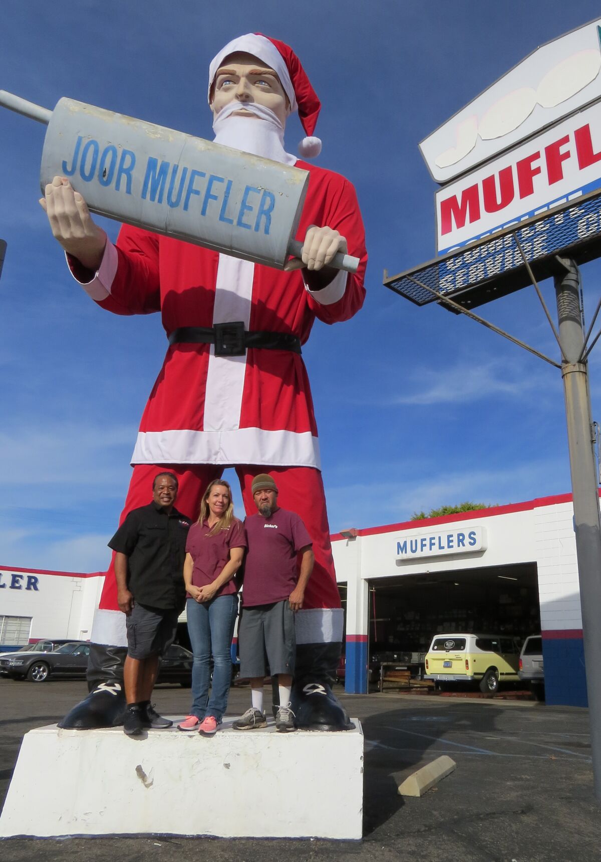 Nick Manning, owner of Joor Muffler & Auto Service, left, with Sickel's Fabrics & Upholstery store co-owners Michelle Guillen and Felix Guillen, pose with the newly costumed Joor Muffler Man in Escondido on Thursday, Dec. 5.