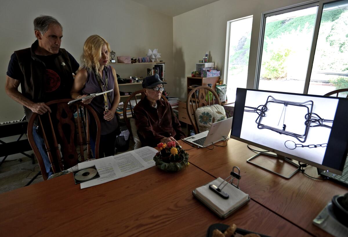 Local residents, from left, Steve Newsom, Allison Kidd and Lien Yang look at photos of an illegal conibear trap similar to one seen on the hind leg of a young local deer, at Newsom's home in La Cañada Flintridge on Tuesday, Oct. 8, 2019. Residents of the area are trying to get the young deer help by contacting local and state authorities.