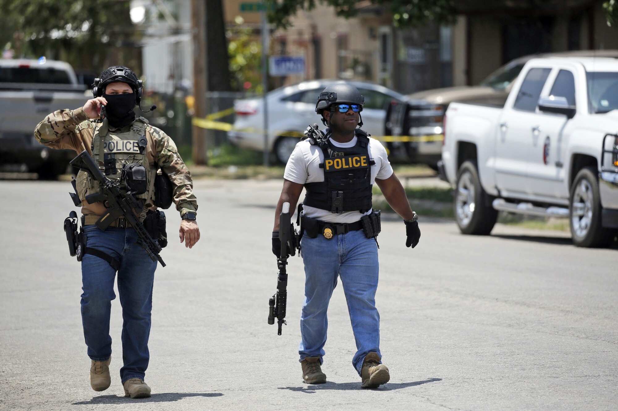 Zwei bewaffnete Personen mit Westen, auf denen die Aufschrift „Polizei“ steht, gehen auf einer Straße 