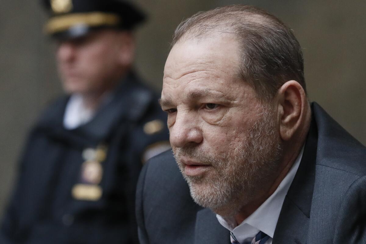 A close-up of Harvey Weinstein with a police officer behind him.