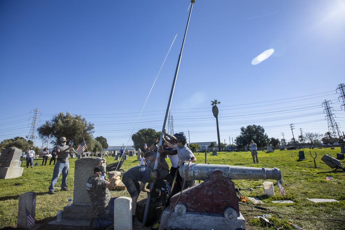 People install a flag pole next to gravestones and a cannon.