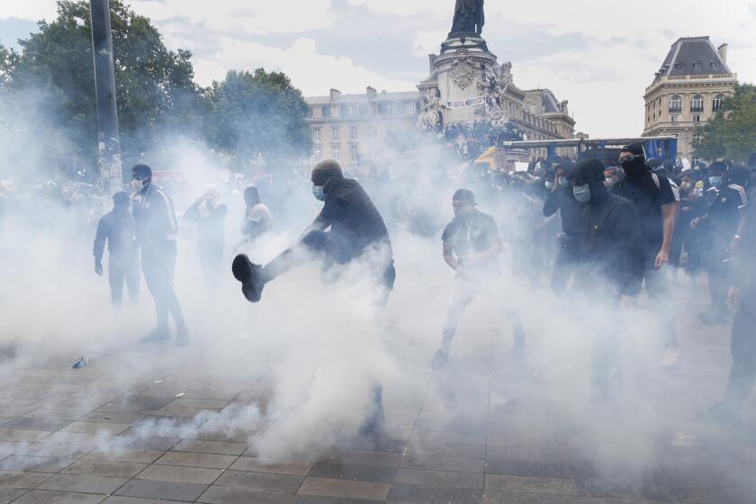 A man kicks a tear gas canister during a march against police brutality and racism in Paris, France, Saturday, June 13, 2020, organized by supporters of Adama Traore, who died in police custody in 2016 in circumstances that remain unclear despite four years of back-and-forth autopsies. The march is expected to be the biggest of several demonstrations Saturday inspired by the Black Lives Matter movement in the U.S., and French police ordered the closure of freshly reopened restaurants and shops along the route fearing possible violence. (AP Photo/Thibault Camus)