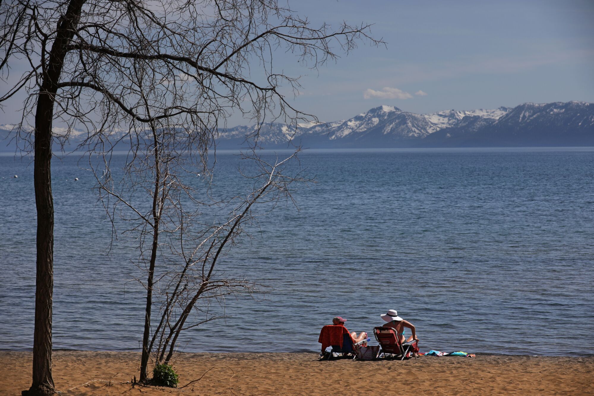 People take in the sun along an empty stretch of sand on the north shore of Lake Tahoe in Kings Beach
