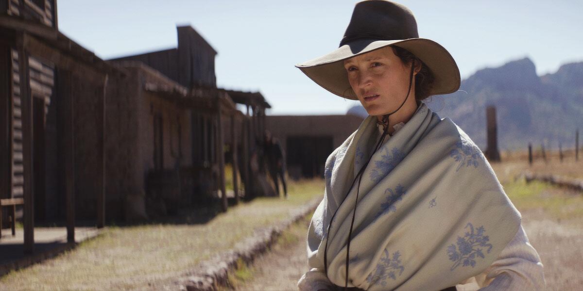 A woman in a hat in a remote town in the Old West.
