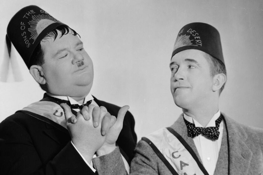 1933: In ceremonial fez and sash, Stan Laurel (1890 - 1965) and Oliver Hardy (1892 - 1957) engage in a masonic-style handshake as they appear in 'Sons Of The Desert', directed by Lloyd French and William A Seiter. (Photo via John Kobal Foundation/Getty Images)
