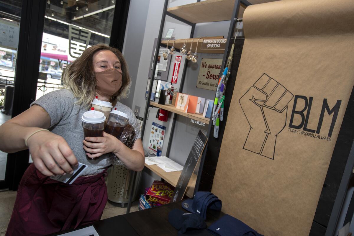 A woman holds a handful of drinks in one arm and a credit card in the other