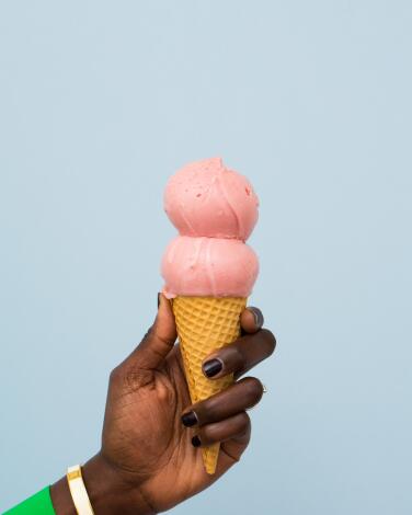 A hand holds up an ice cream cone topped with two perfectly round pink scoops