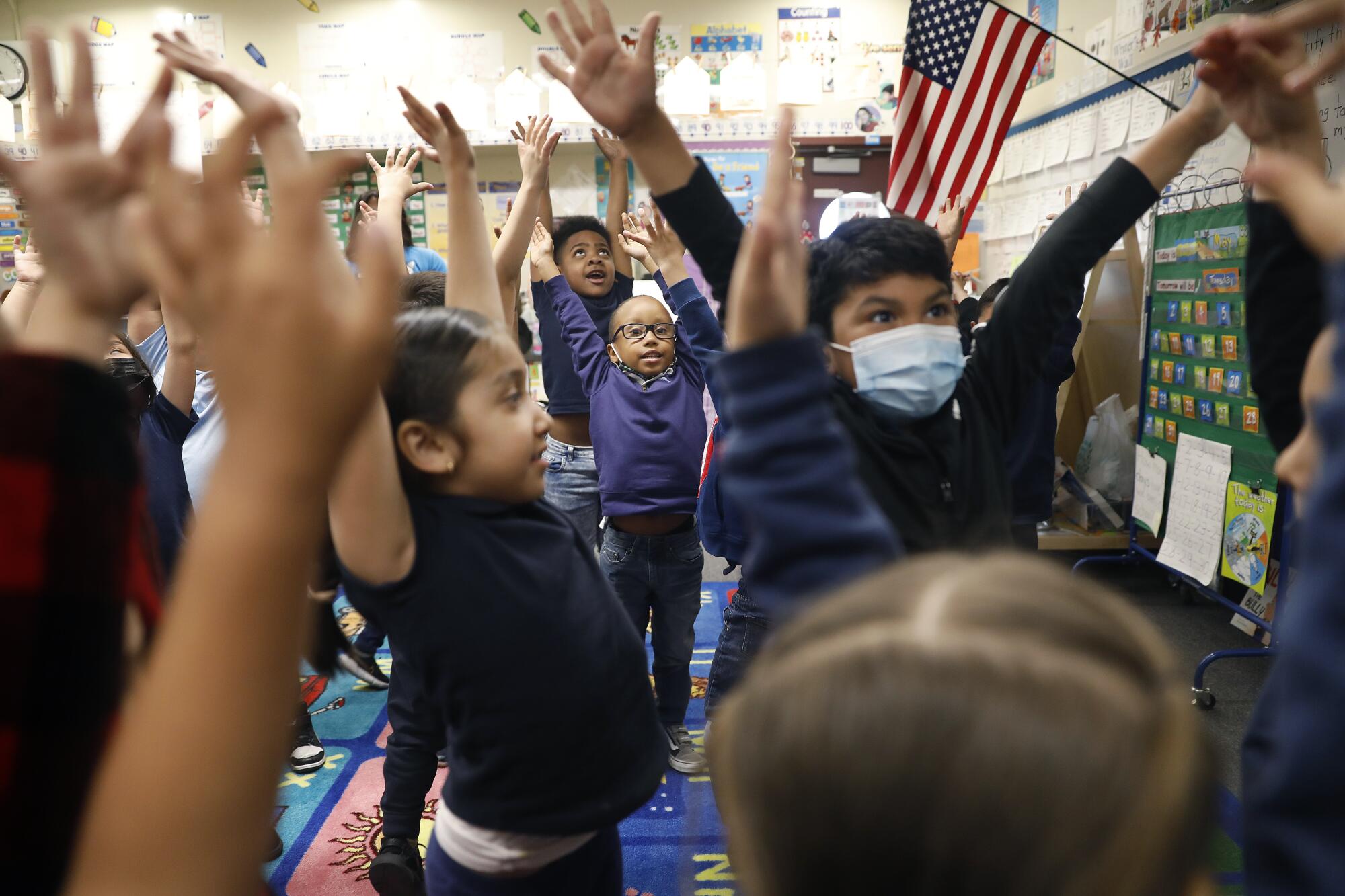 Small children raise their arms in a classroom.