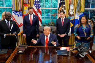 People stand around President Trump in the Oval Office
