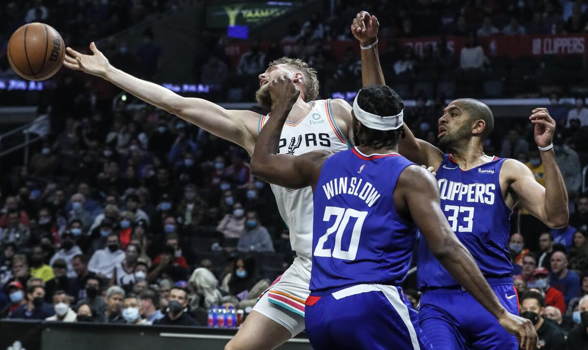 San Antonio Spurs' Jock Landale stretches for a rebound as Clippers' Justise Winslow and Nicolas Batum look on.