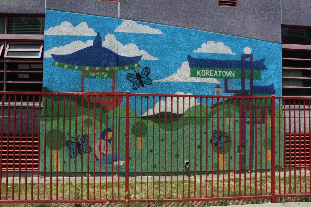 A mural on a school wall is behind a red gate. 