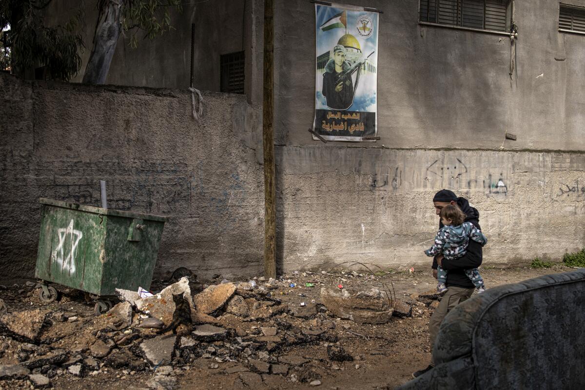 A Palestinian man carries a child down a damaged road
