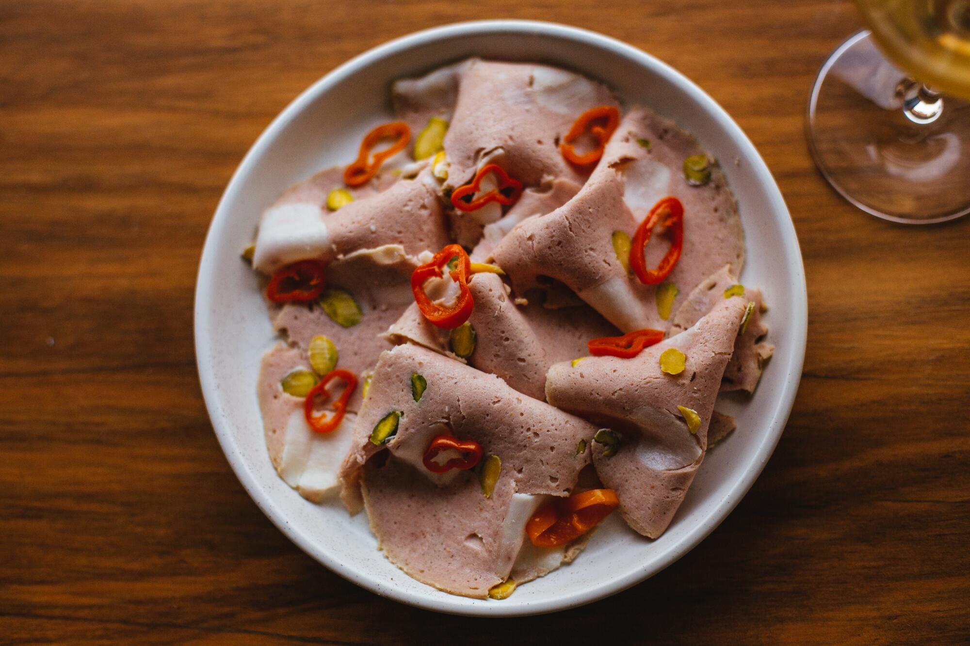 Slices of mortadella with sliced chili peppers scattered over them.