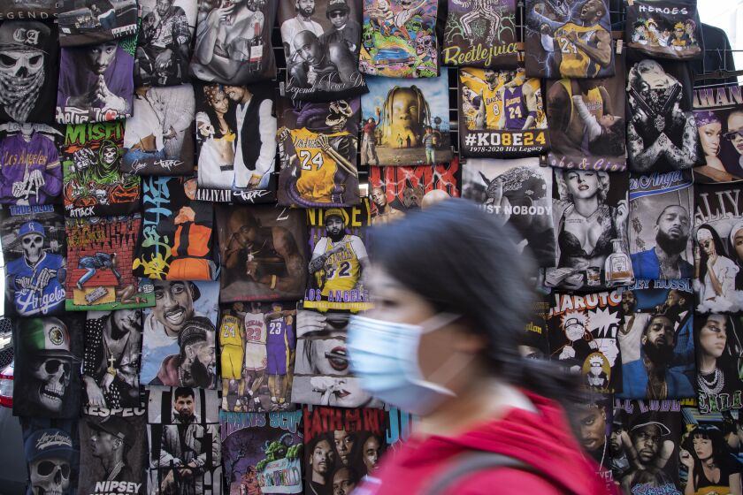 LOS ANGELES, CA - DECEMBER 20: A masked shopper passes a wall of t-shirts in the Fashion District on Monday, Dec. 20, 2021. Health officials are warning of a possible winter COVID surge with the Omicron variant. (Myung J. Chun / Los Angeles Times)
