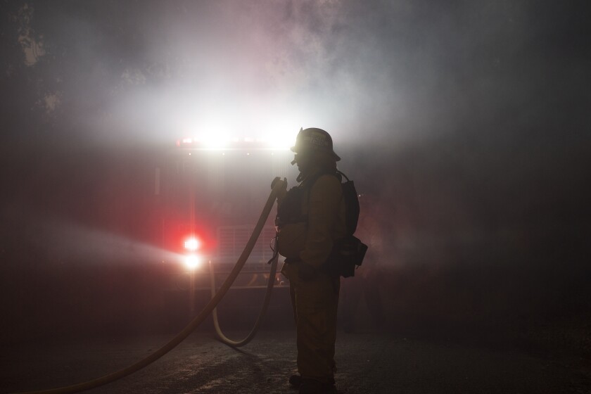 A firefighter holds a hose amid the Carmel Fire near Carmel Valley, Aug. 18, 2020.