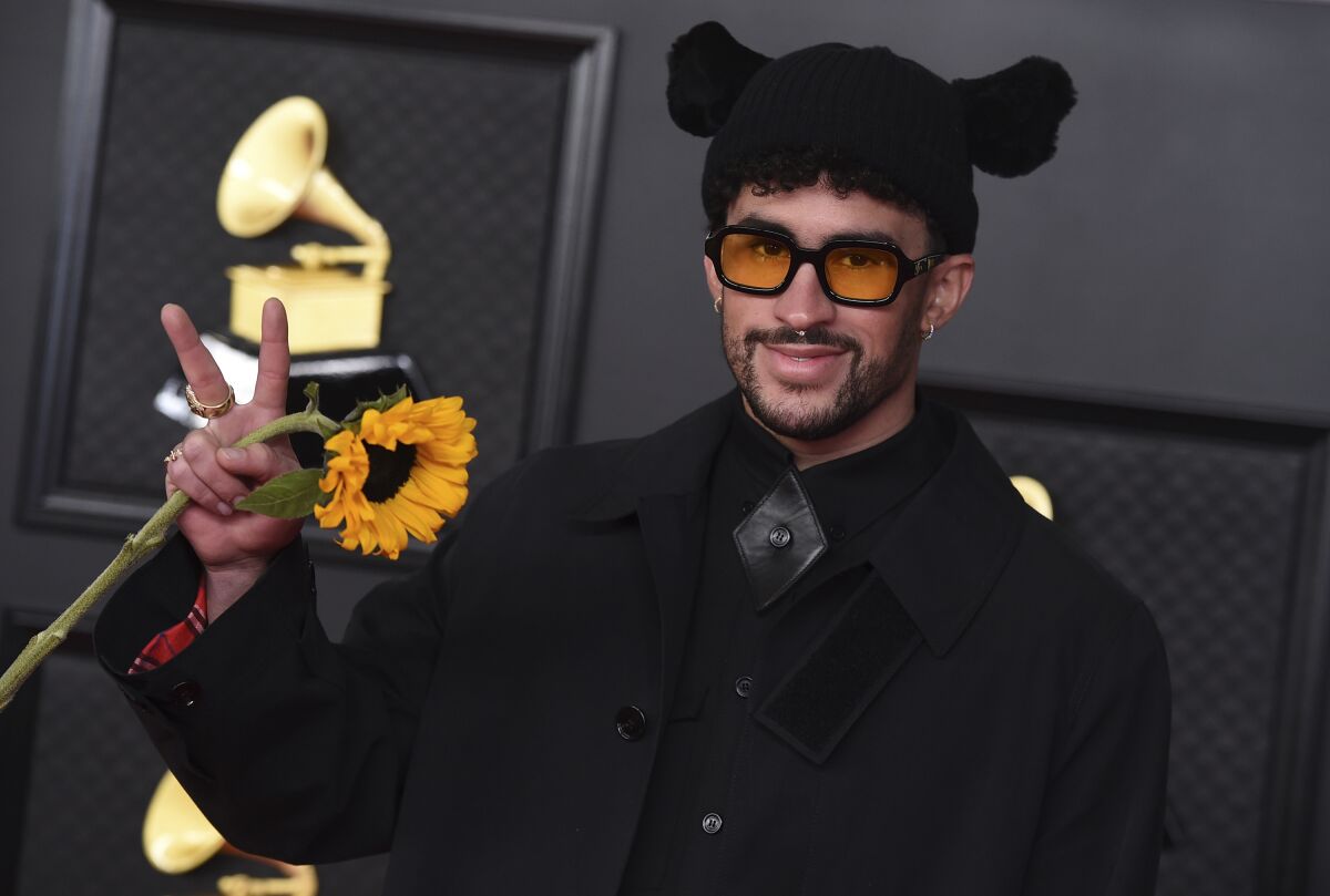 A man wearing a black hat with ears and making a peace sign with a sunflower in his hand