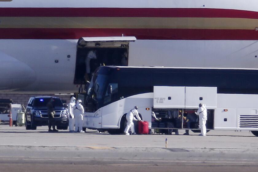 Personnel in protective clothing unload luggages from the airplane carrying U.S. citizens being evacuated from Wuhan, China, at March Air Reserve Base in Riverside, Calif. Jan. 29, 2020. (AP Photo/Ringo H.W. Chiu)