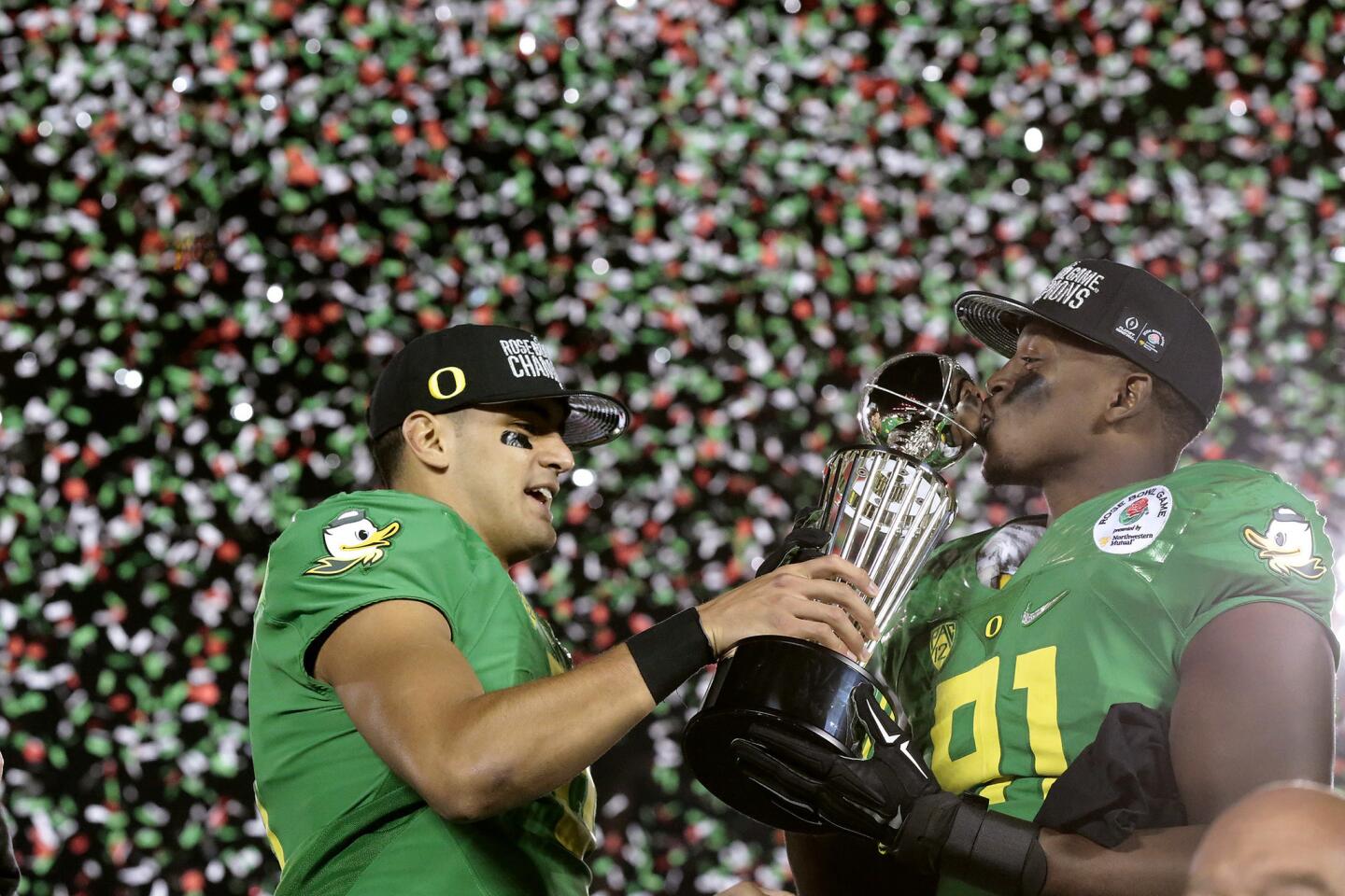 Oregon quarterback Marcus Mariota hands the Rose Bowl's Leishman Trophy to linebacker Tony Washington, who gives it a kiss, after the Ducks defeated Florida State in a College Football Playoff semifinal.