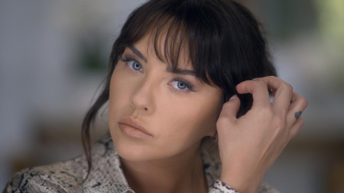 A woman with blue eyes brushing her brown hair back over her ear