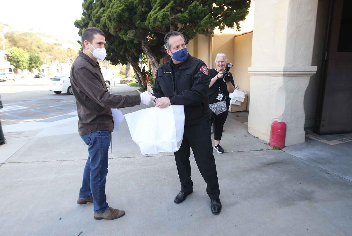 Laguna Beach Fire Chief Michael Garcia, right, is given bags of prepared meals from Frontline Foods' Eric Paine on Monday in observance of International Firefighters Day.