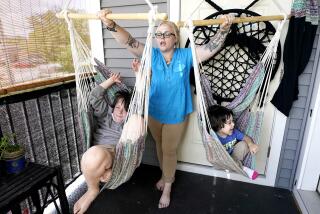 A blond woman plays with two children in swings on a porch of a home.