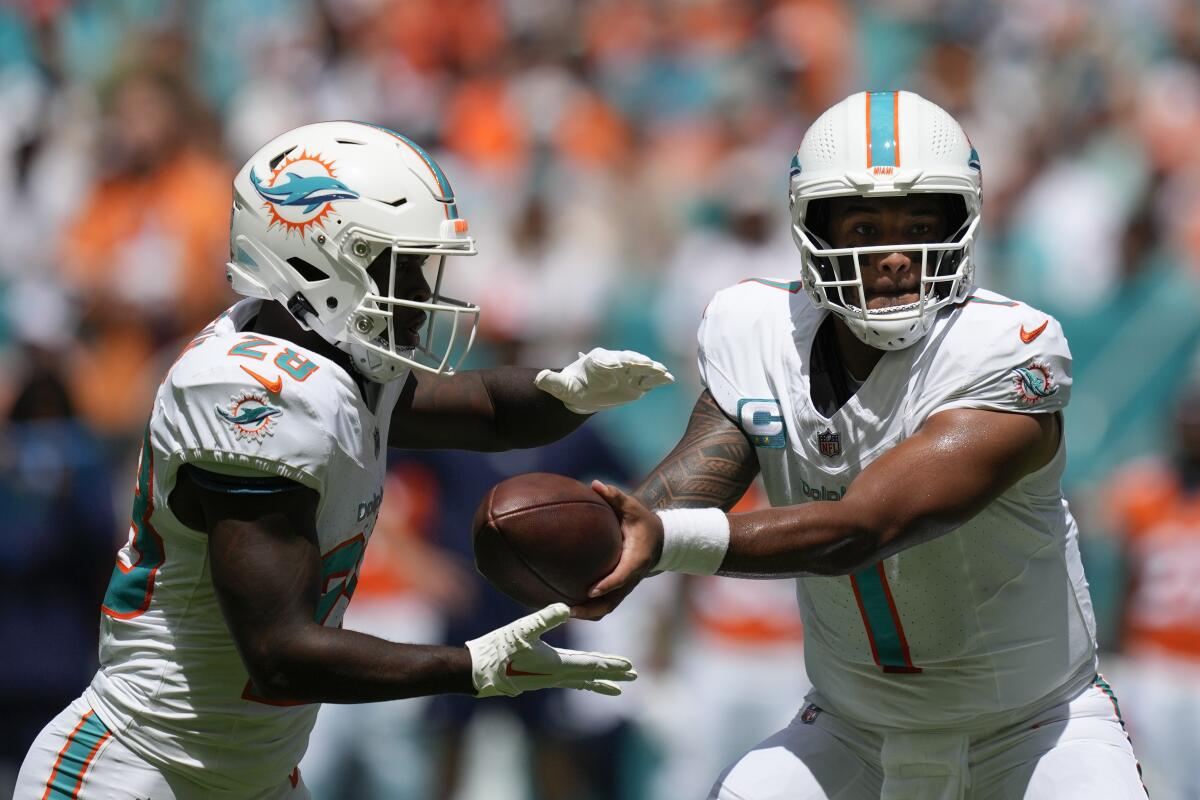 Miami Dolphins quarterback Tua Tagovailoa hands off the ball to running back De'Von Achane.