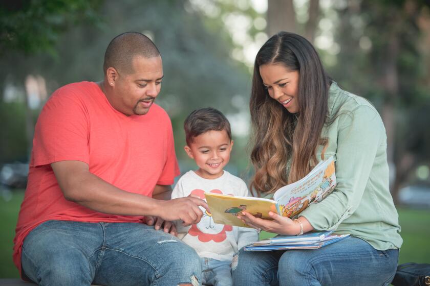 A man and a woman read a picture book to a young boy, who sits between them.