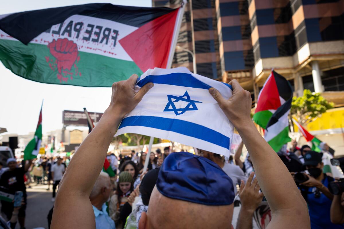 A man wearing a yarmulke holds a small Israeli flag over his head as pro-Palestinian supporters march.