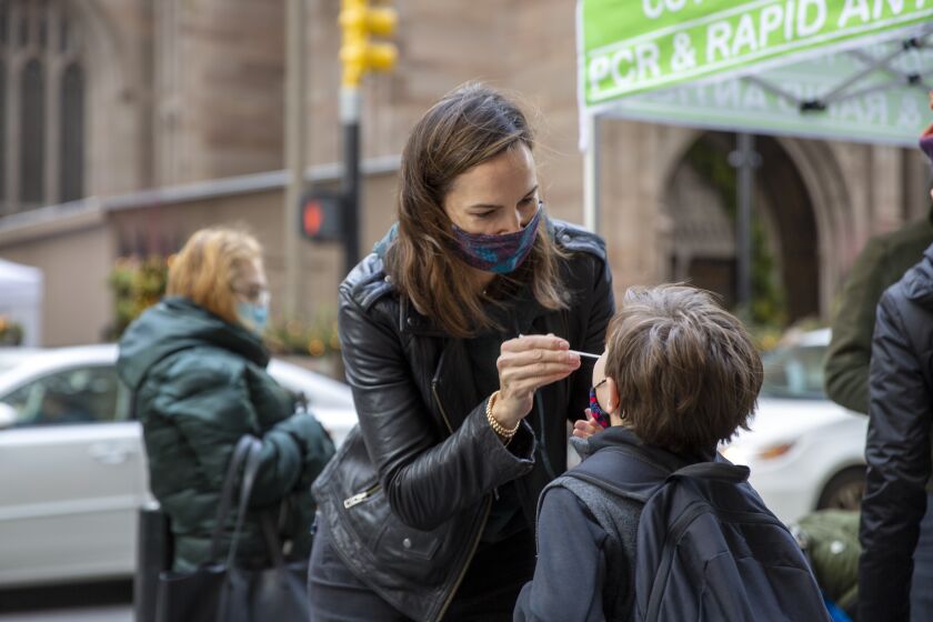 FILE - Katie Lucey administers a COVID-19 test on her son Maguire at a PCR and Rapid Antigen COVID-19 coronavirus test pop up on Wall Street in New York on Thursday, Dec. 16, 2021. U.S. health officials are endorsing ‘test-to-stay’ policies that will allow close contacts of infected students to remain in classrooms. The Centers for Disease Control and Prevention on Friday, Dec. 17, decided to more firmly embrace the approach, after research of such policies in the Chicago and Los Angeles areas found COVID-19 infections did not increase when schools switched to test-to-stay. (AP Photo/Ted Shaffrey)
