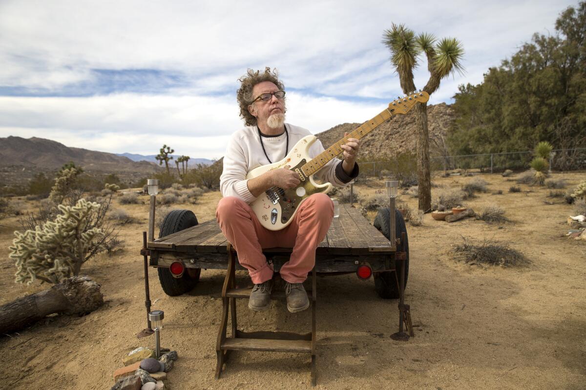 Joshua Tree musician Robbi Robb strums his Fender Stratocaster on an old trailer overlooking Joshua Tree landscape.