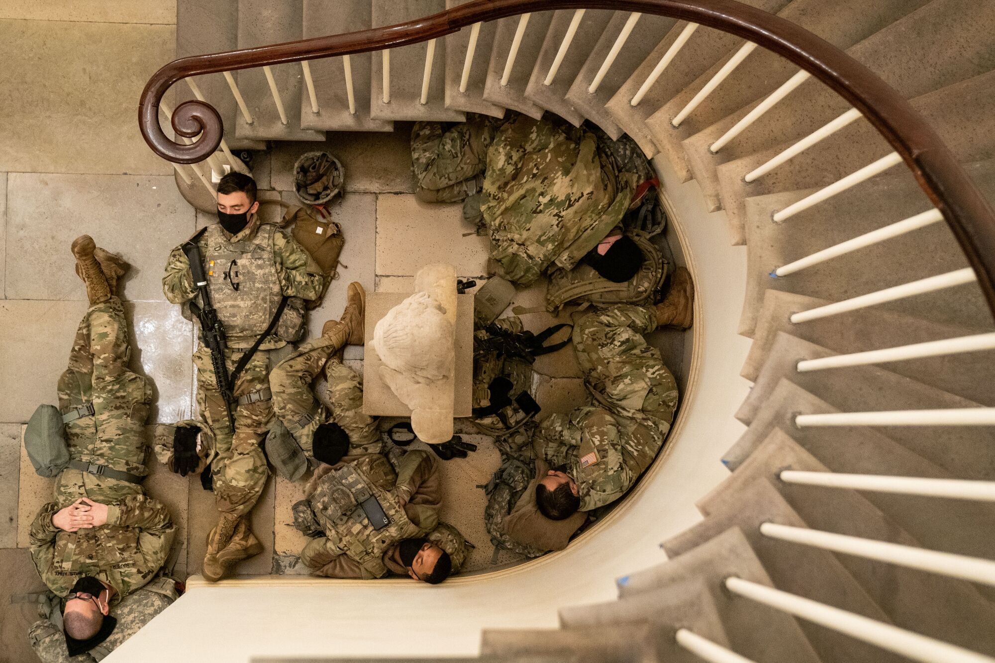 Service members in uniform sleep in an alcove below a curved stair