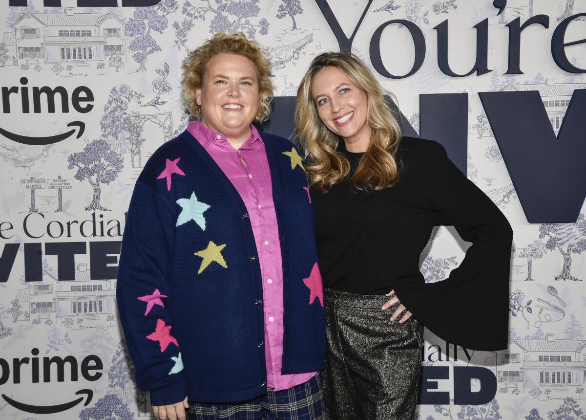 Fortune Feimster in a blue cardigan with stars in many colors stands with her arm around Jacquelyn Smith, who has long hair