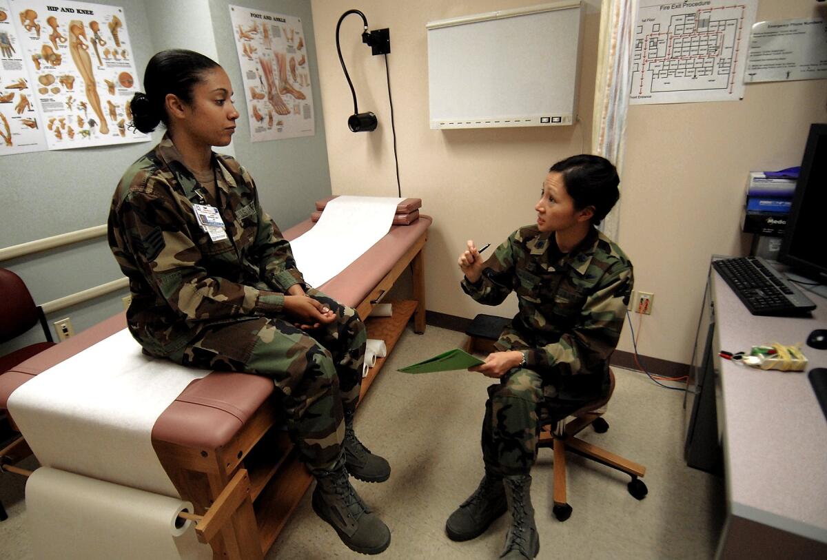 A military doctor speaks with a patient in an exam room.