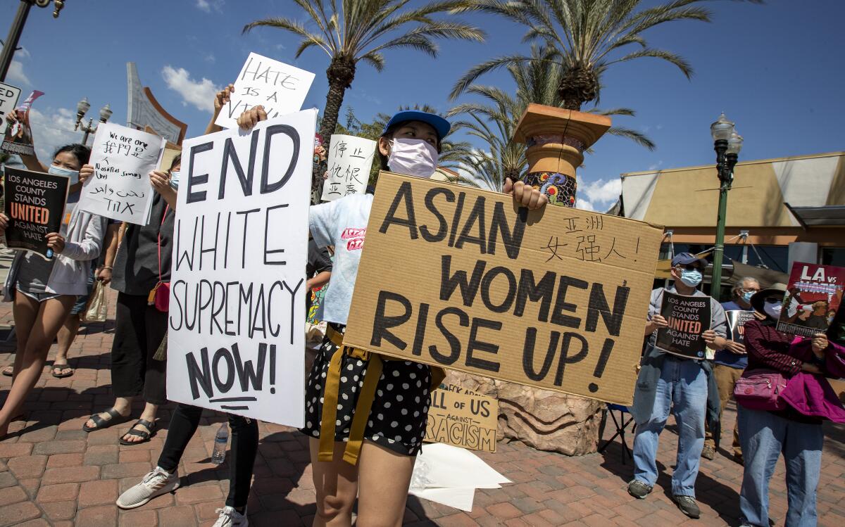 A demonstrator holds signs that read "End white supremacy now!" and "Asian women rise up!" at a rally.