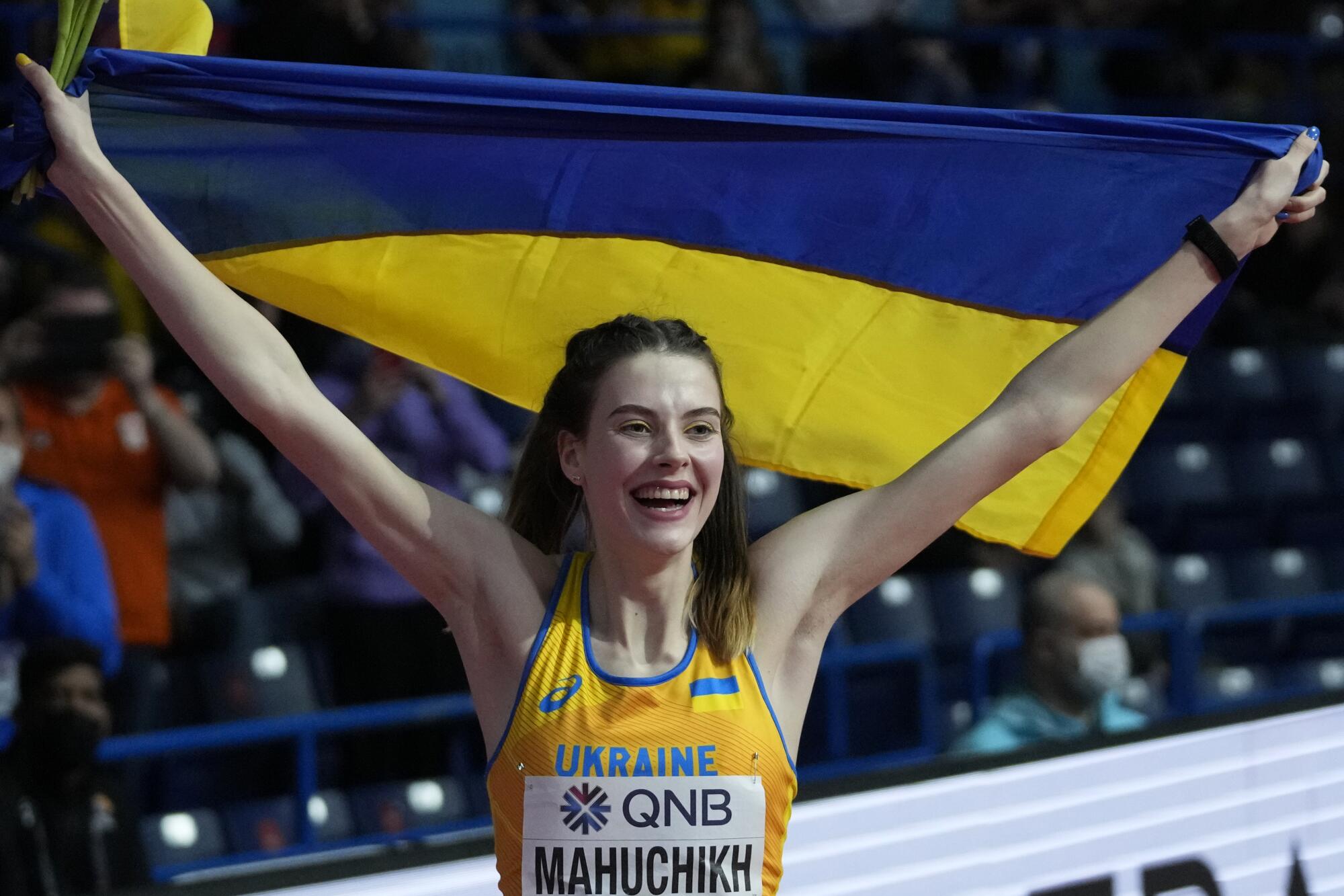 Yaroslava Mahuchikh celebrates by raising the Ukrainian flag after winning the high jump at the world indoor championships.