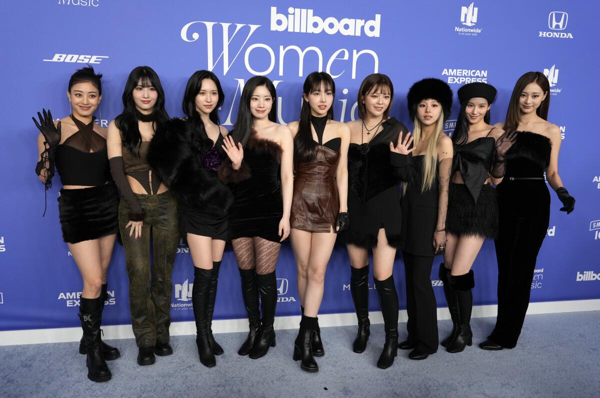 Nine young women wearing black outfits stand and pose in front of a blue backdrop.