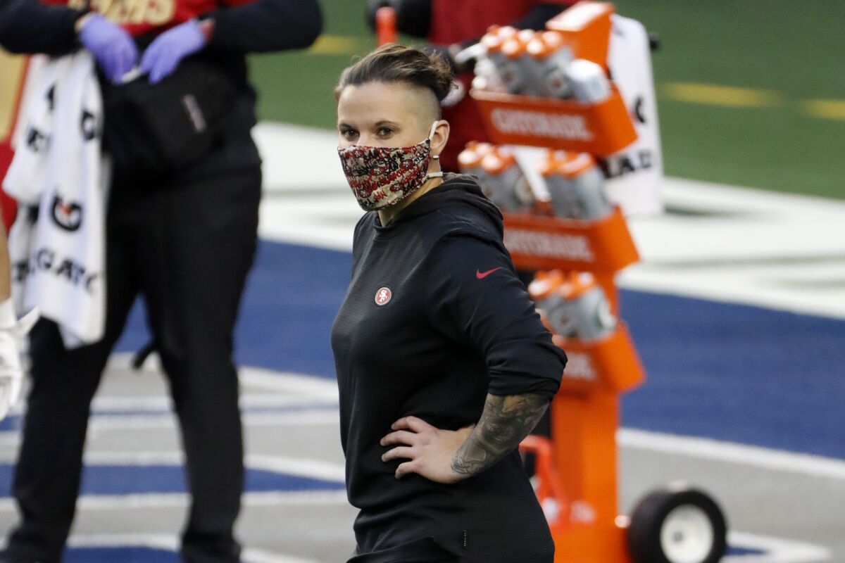 FILE - In this Dec. 20, 2020, file photo, San Francisco 49ers offensive assistant Katie Sowers stands on the field during warmups before an NFL football game against the Dallas Cowboys in Arlington, Texas. Sowers will not be returning to the 49ers in 2021 after becoming the first female coach to make it to the Super Bowl last year. A person familiar with the situation said the 34-year-old Sowers will leaving coach Kyle Shanahan’s staff where she worked closely with receivers coach Wes Welker. The person spoke on condition of anonymity because the team had not made an announcement. (AP Photo/Roger Steinman, File)