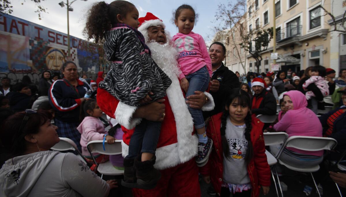 Santa (Jorge Grajeda of Pomona) carries Angelica Romero, 4, left, of Hawaiian Gardens and Maya Epps, 5, of Pomona as he leads a crowd to the toy giveaway at Fred Jordan Mission in Los Angeles in 2013.