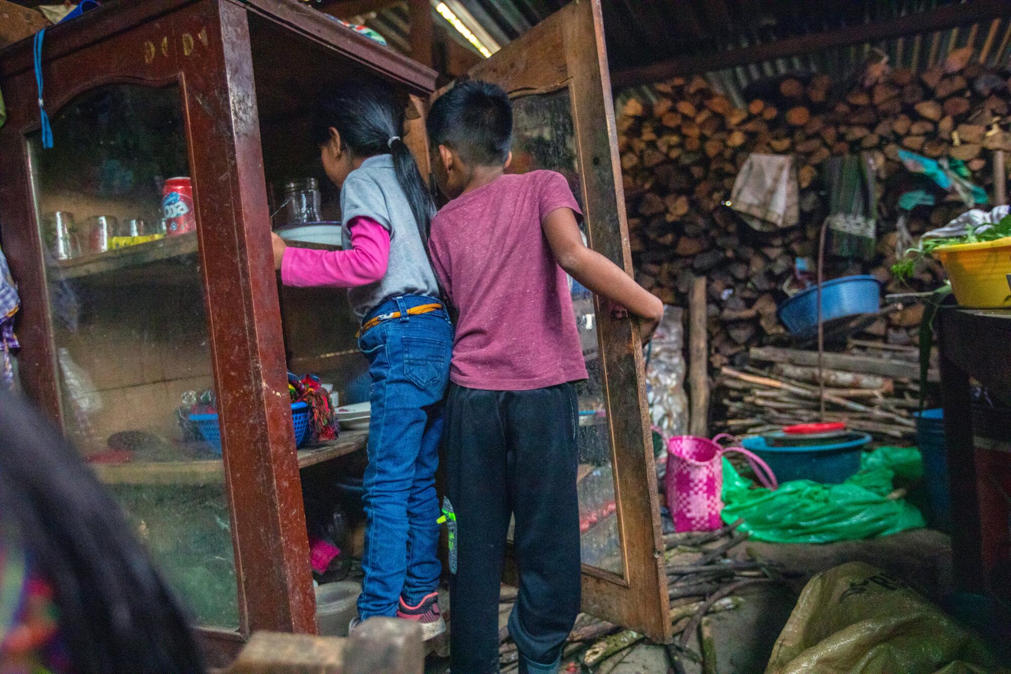 A young girl, left, and a boy check out the contents of a cabinet inset with glass near stacks of firewood