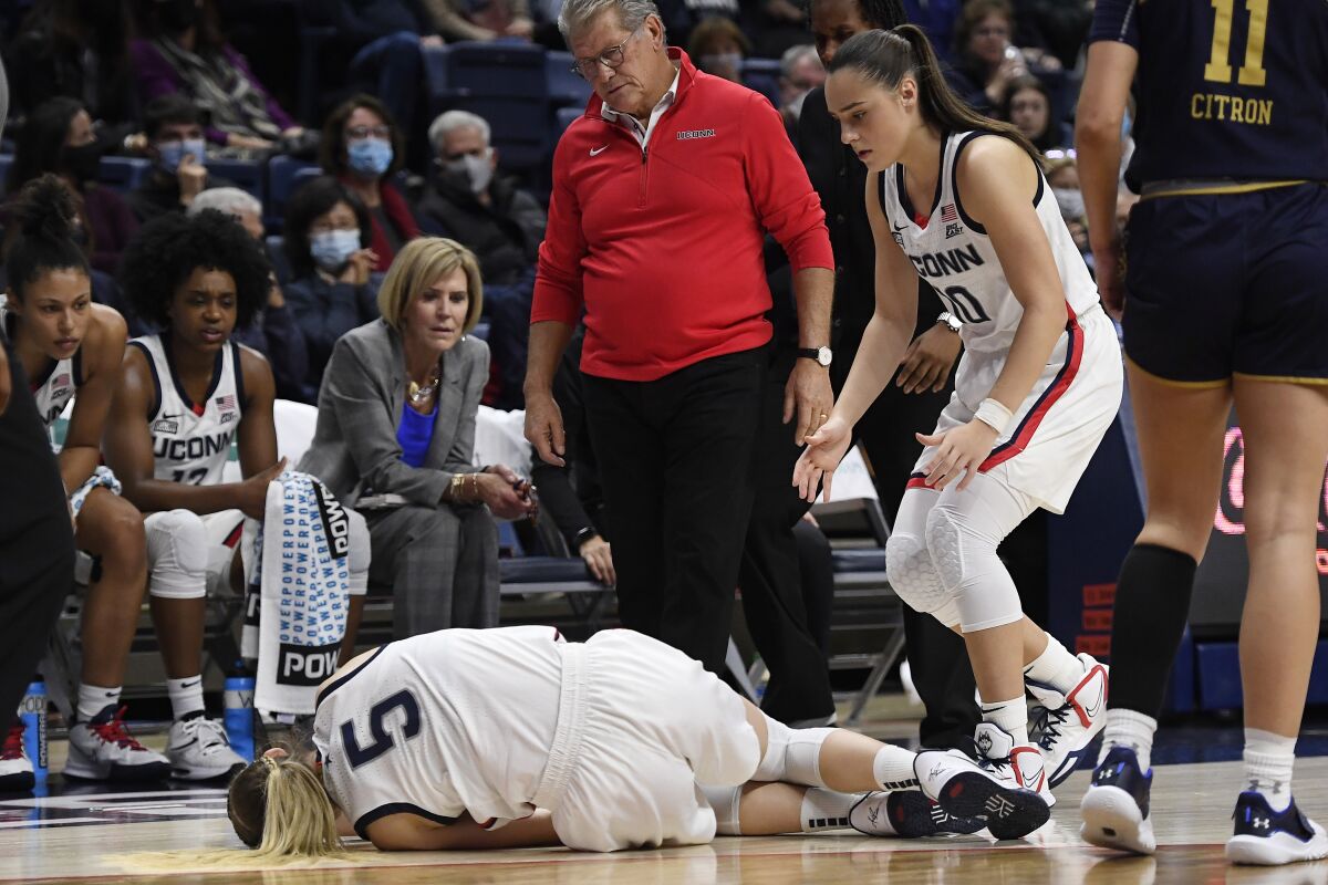 Connecticut's Paige Bueckers stumbles injured as Connecticut's Nika Mühl and head coach Geno Auriemma looks on the second half of an NCAA college basketball game against Notre Dame, Sunday, Dec. 5, 2021, in Storrs, Conn. (AP Photo/Jessica Hill)