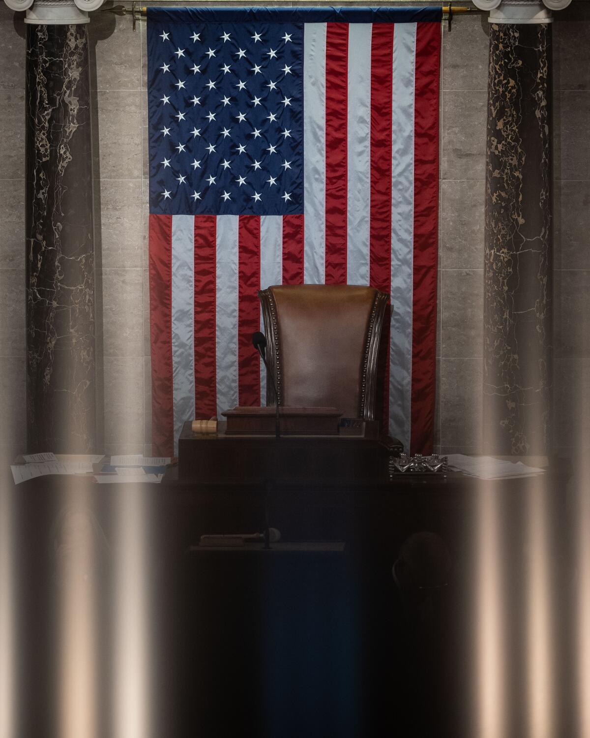 An empty chair sits in front of an American flag.