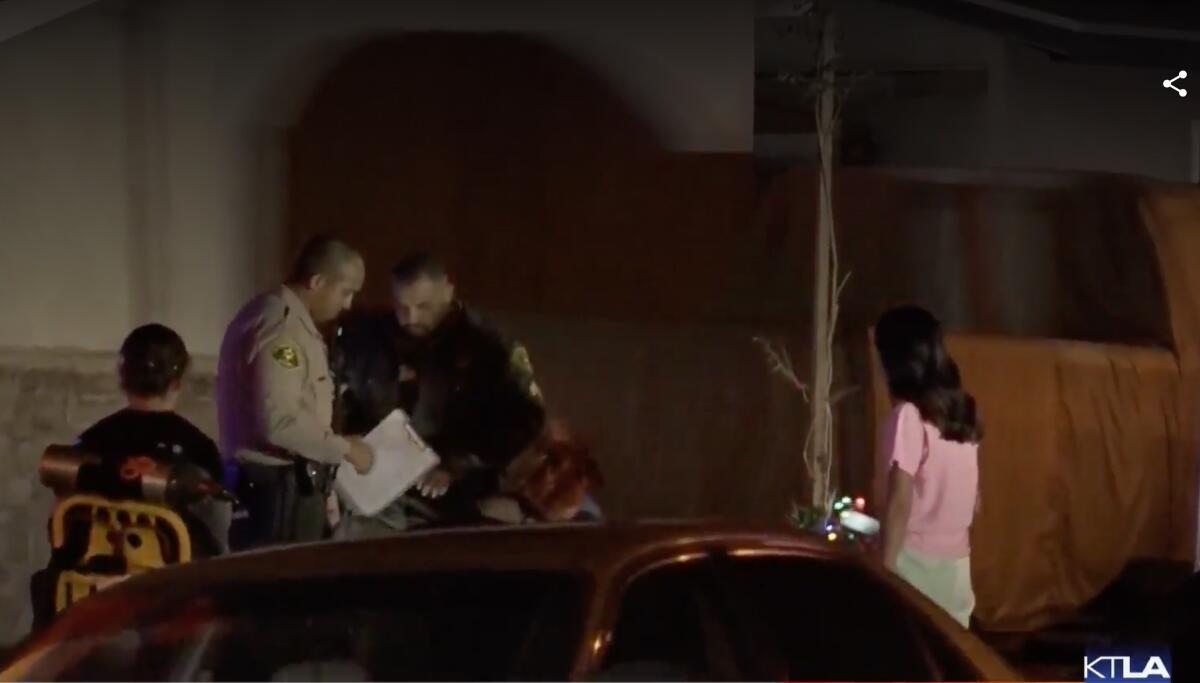 Law enforcement and other people stand outside a house at night.