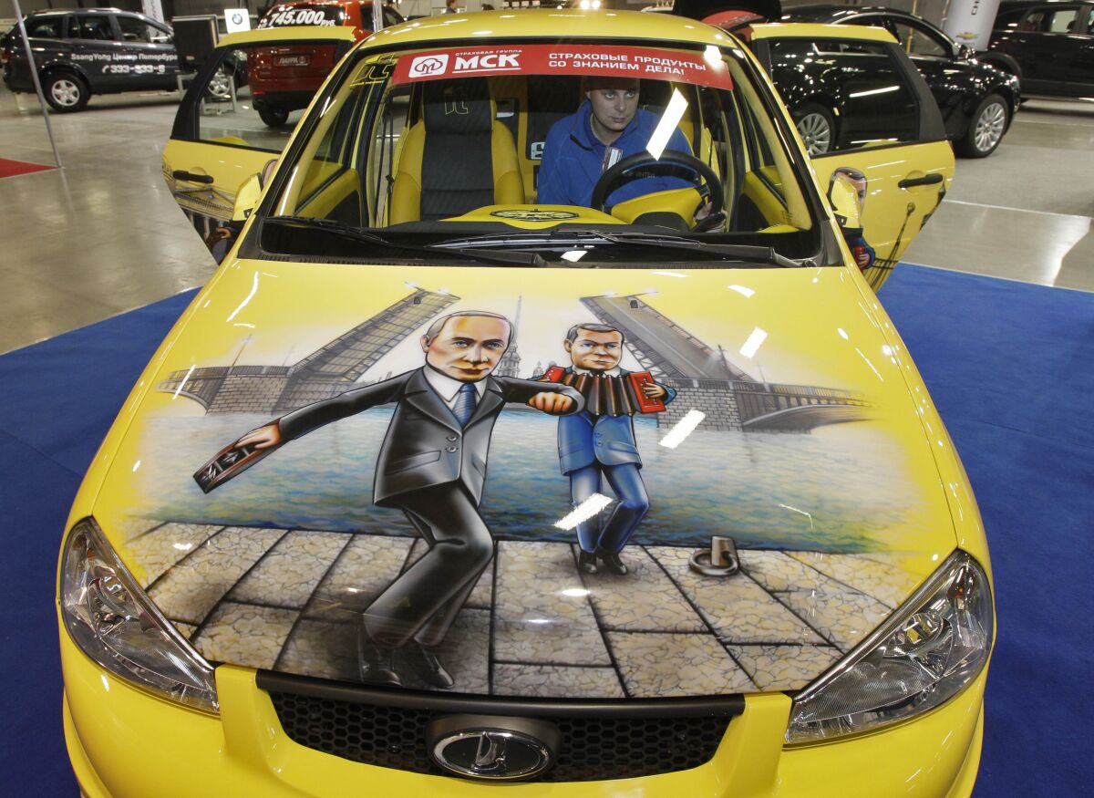 FILE - In this Oct. 21, 2011 file photo, a man sits in a Russian made Lada Kalina sports car with a depiction of Russian Prime Minister Vladimir Putin, left, and Russian President Dmitry Medvedev painted on the bonnet, at a car tuning company's stand during an automotive exhibition in St. Petersburg, Russia. Russia will take control of French car manufacturer Renault’s operations in the country and resurrect a Soviet-era auto brand. The news Monday marks the first major nationalization of a foreign business since the war with Ukraine began. Renault says it would sell its majority stake in Avtovaz to a state-run research institute known as NAMI. Avtovaz is best known for its Lada brand. (AP Photo/file)