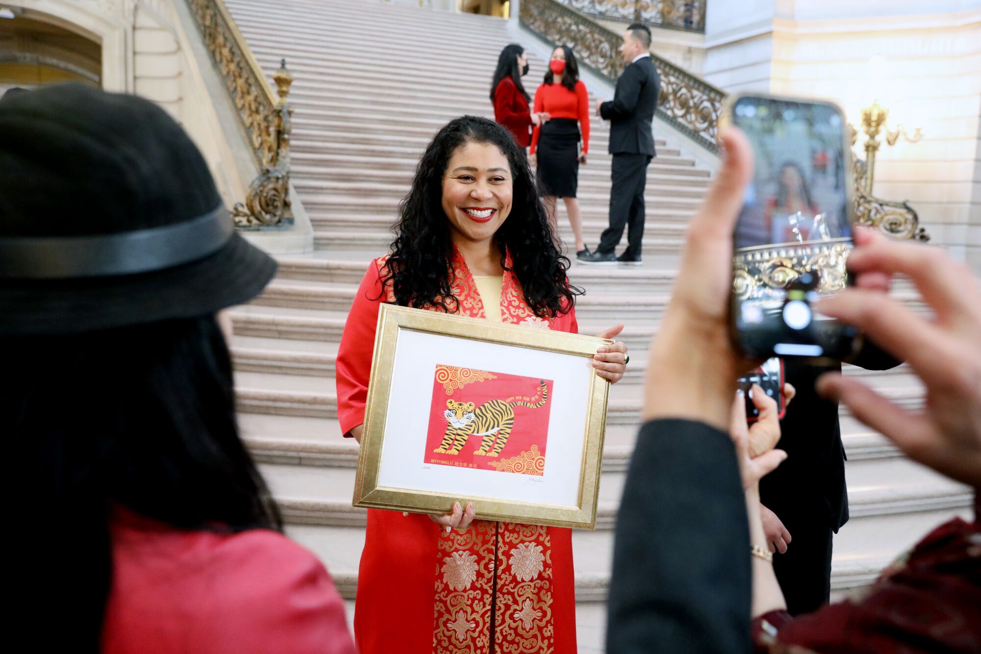 London Breed poses for photos at the bottom of a large flight of stairs while holding a picture of a tiger 