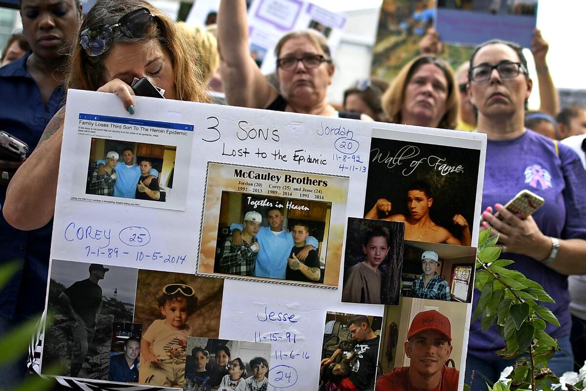A woman holds a sign with photos of three sons.