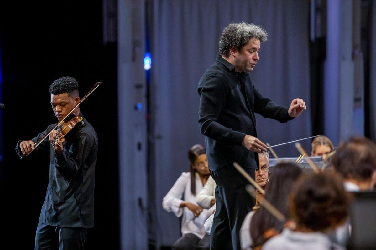 A standing violinist performs as a conductor leads a seated orchestra