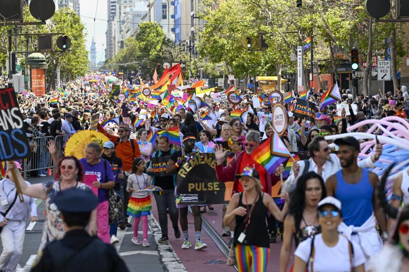 Dozens of SF Pride parade attendees walking down Market Street waving pride flags 