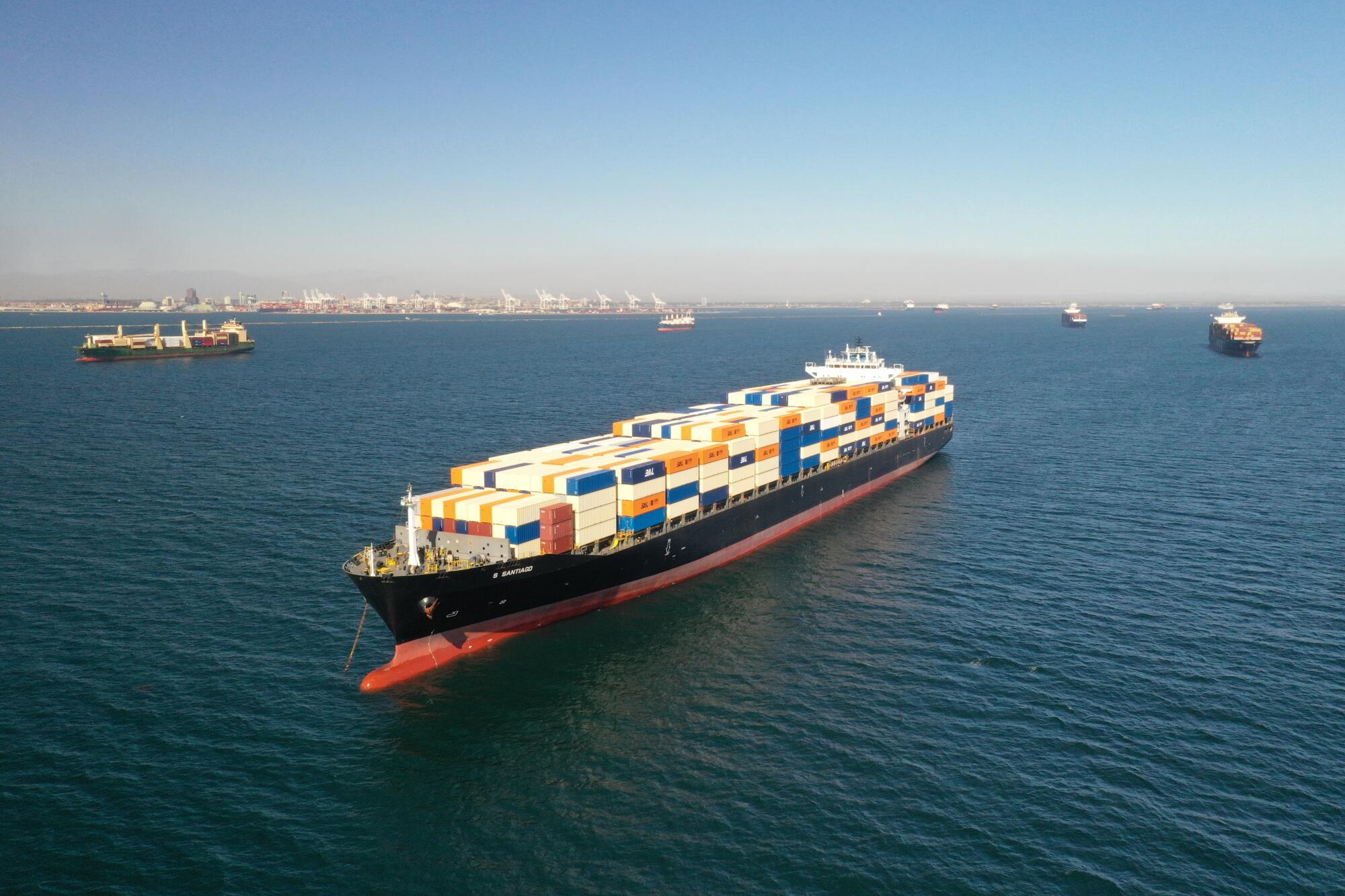 A cargo ship laden with containers sits at sea. In the distance are other vessels.